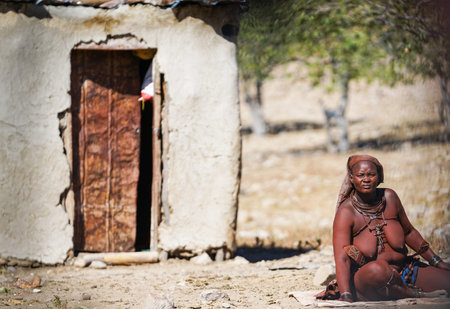 DAMARALAND NAMIBIA - MAY 21 2018; Tribal woman with traditional necklaces and adornments sits on mat...