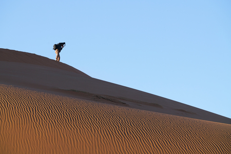 SOSSUSVLEI, NAMIBIA - MAY 18 2018; Tourist photographer in distance on ridge on dunes of Hidden Vlei against blue sky  Sossusvlei Namibiaのeditorial素材