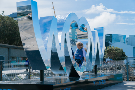 WELLINGTON, NEW ZEALAND - OCTOBER 1 Child plays in centre heart shaped O in World of Wearable Art iconic shiny silver sign on city waterfront reflects city and arbour scenesのeditorial素材