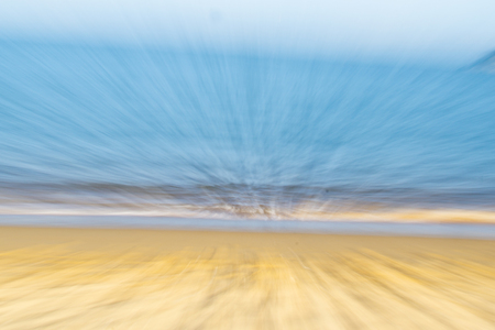 Coastal abstract golden sand blue water and pale sky in zoom blur for backgroundsの写真素材