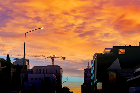 Urban skyiline in silhouette with heavy colorful clouds overhead and construction crane above buildings as city of Christchurch redevelops post earthquakeの写真素材