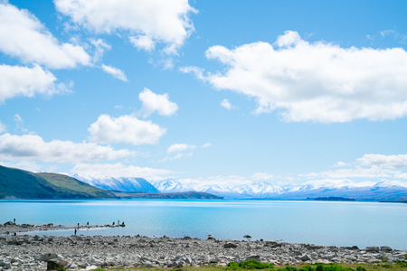 LAKE TEKAPO NEW ZEALAND - OCTOBER 14 2018;Expansive views turquoise water of Lake Tekapo with snow-capped Southern Alps behind and tourists on rocky foreshoreのeditorial素材
