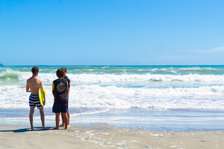 MOUNT MAUNGANUI NEW ZEALAND - FEBRUARY 10 2019: Teenagers standing together talking by water's edgeのeditorial素材