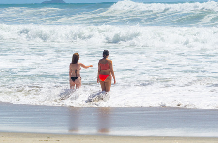 MOUNT MAUNGANUI NEW ZEALAND - FEBRUARY 10 2019: Young women at beach entering surf with large and dangerous sea enjoying summer day outdoors.のeditorial素材