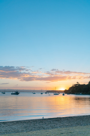 Scenic vista as sun sets over Pilot Bay on Tauranga Harbour with silhouette of boats and Mount Maunganuiの写真素材