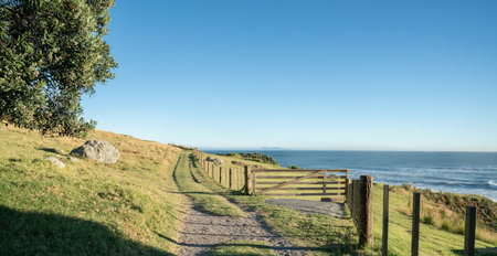 Track along fenceline past closed farm gate on slpoing hillside with view out to sea and horizon.
