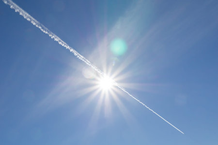 Jet stream through sun with lens flare in abstract blue sky