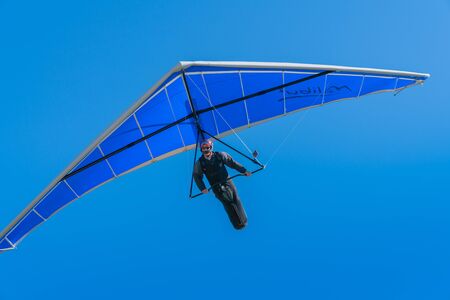 TAURANGA NEW ZEALAND - FRBRUARY 9 2019; Hang glider pilot flying towards under bright blue wing and sky.のeditorial素材