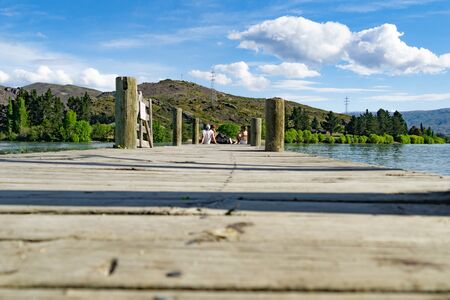 CROMWELL, NEW ZEALAND - OCTOBER 21 2019;  Group four youth sitting socializing  on end of pier on Lake Dunstanのeditorial素材