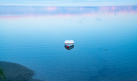 White dinghy afloat on calm blue water with reflection of sunset colors  in tranquil scene.の写真素材