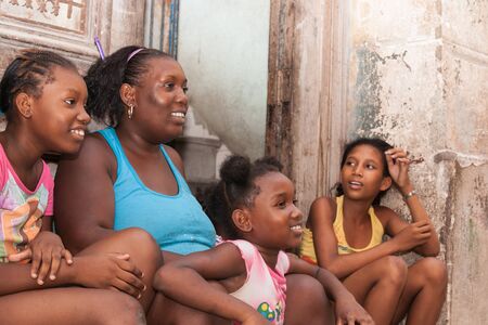 HAVANA CUBA - JULY 7 2012; Mother and three daughter sit on doorstep on street in happy and smiling in front dilapidated wall and door.のeditorial素材