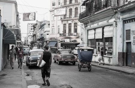 HAVANA CUBA - JULY 8 2012; Street in Havana with people walking to and fro, classic American vehicles and old dilapidated buildings desaturated color.のeditorial素材