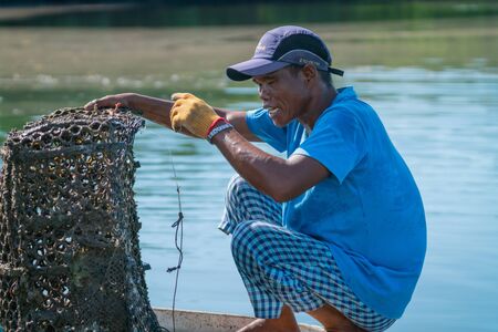 LAHAD DATU MALAYSIA - MAY 17 2019; Fisherman in small boat and blue shirt searches out his fish traps in shallow harbor.のeditorial素材