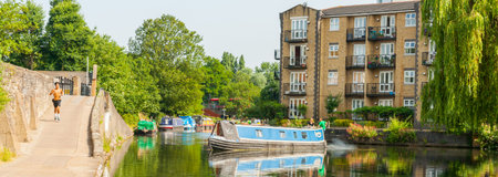 LONDON ENGLAND - JULY 13 2013; Travellers in river barge turn it in Regents Canal as young man runs...
