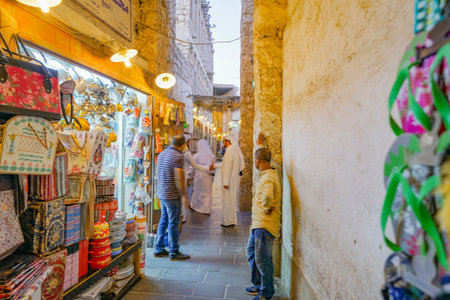 DOHA QATAR - JULY 11 2019; Focus on Arabic man in customary white robes in lane among market vendors and products and ambience of Souq Waqifのeditorial素材