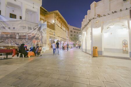DOHA QATAR - JULY 11 2019; Night scene long exposure in Souq Waqif with women sitting at table while people bluured in motion walking pastのeditorial素材
