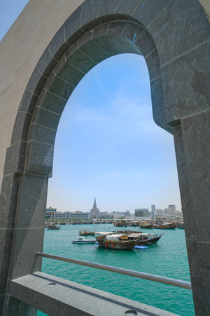 Outside architectural arch on Museum of Islamic Arts with view across Doha Boat harbor to city...