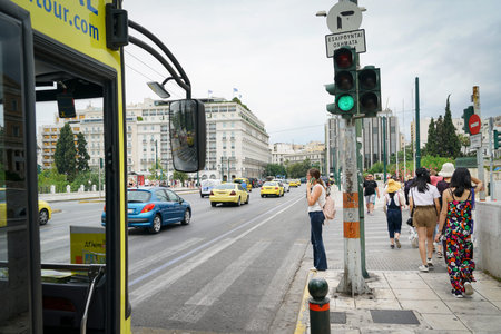 ATHENS GREECE - JULY 15 2019; Woman waiting at pedestrian crossing talking on mobile phone while vehicles and a bus passのeditorial素材