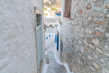 Hydra, Greek Island - July 20 2019; Narrow alley down to balcony restaurant with white washed walls and blue windows and decorations.