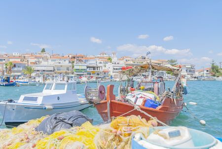 Ermioni Greece - July 20 2019; waterfront with orange boat in foreground and its quaint fishing boats moored along pier and town buildings behind.のeditorial素材
