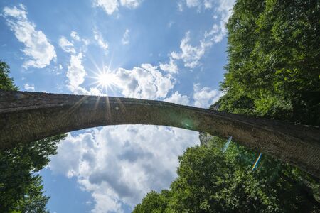 Below historic stone single arch pedestrian bridge looking up to sky at Zagori in mountains in central Greece.の写真素材