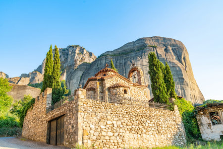 Large imposing rocks rise behind quaint Greek Orthodox stone church in town of Kastraki, Meteora...