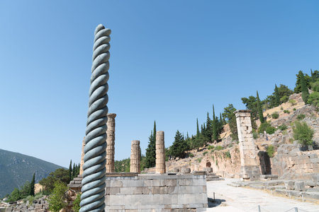 Delphi Greece - July 28 2019; Ancient city of Delphi remains of serpent column among ruins and...