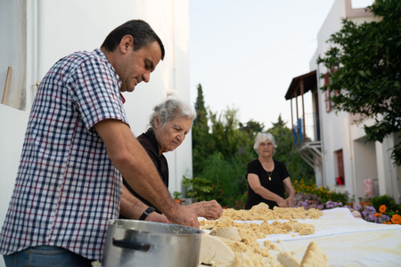 Skiathos Greece - August 2 2019; People, two senior women and man in selective focus preparing dough, kneeding on outdoor table.のeditorial素材