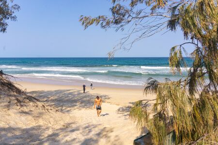 Surfers aaparadise, Australia - November 17 2019; Bare-chested man leaving beach while a couple of tourists near the ocean beach framed by trees take photos.のeditorial素材