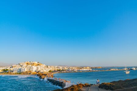 naxos Greece - August 12 2019; Buildings clustered over hill of Naxos Town and people crossing over to the Temple Of Apollo being splashed by sea.のeditorial素材