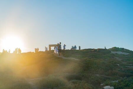 Naxos Greece - August 12 2019; Tourists walking up to Temple of Apollo for the sunset back-lit by sun approaching the top of hill.のeditorial素材