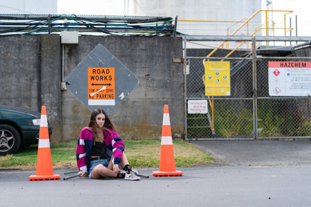 Teenager sitting bewteen road cones in front of no parking sign in Auckland city industrial area.