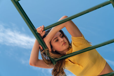 Teenage girl on resting on children's playground equipment with blue sky