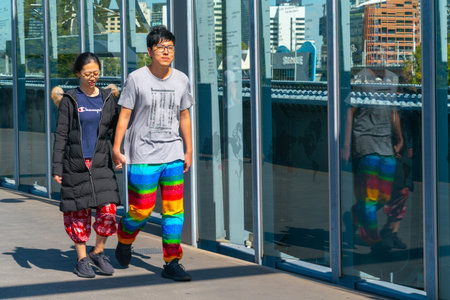 Melbourne Australia - March 10 2019; Asian tourist couple on Sandridge pedestrian bridge passing the huge stainless sculptures and glass panels telling history of immigrants to Australia.のeditorial素材