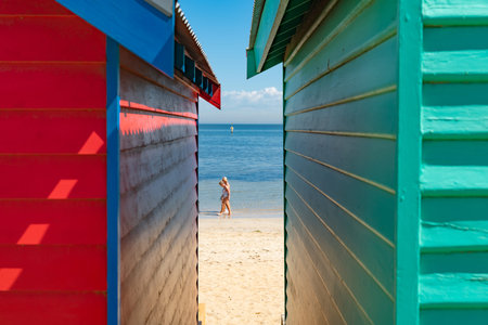 Melbourne Australia - March 11 2020; View between colourful Brighton Beach boxes to water's edge with two people walking along.のeditorial素材