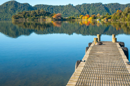 lake Tarawera view from jetty across lake to autumn colors and surrounding tree clad hills.の写真素材