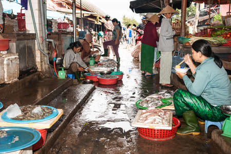 Hoi An Vietnam October 19 2013; Typical wet markets  in Asian city with vendors preparing their offerings and waiting for customers while one woman sits eating amongst the  wet food and produce.のeditorial素材