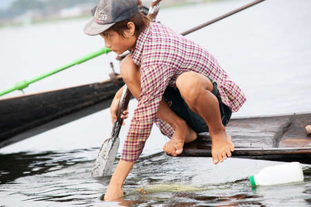 Inle Lake Myanmar - November 2 2013; Portrait of fisherman on end of traditional long boat swishing water .1のeditorial素材