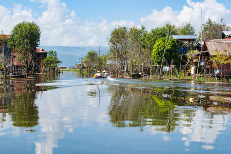 Inle Lake Myanmar - November 2 2013; Inle Lake locals motoring in small boat up channel between homes of floating village.のeditorial素材