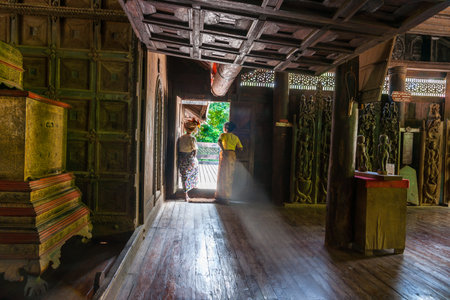 Sa Lay Myanmar - October 31 2013; Two women in dratitional dress standing back-lit by light entering doorway in Yokesone Monastery historic wooden Buddhist monastery constructed in teak around 1882 now a museum.のeditorial素材