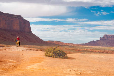 Utah USA - September 23 2015; Cowboy on horseback on red rock ledge inMonument Valley among imposing geological rock structures of geological rock outcrops in Utah USAの写真素材