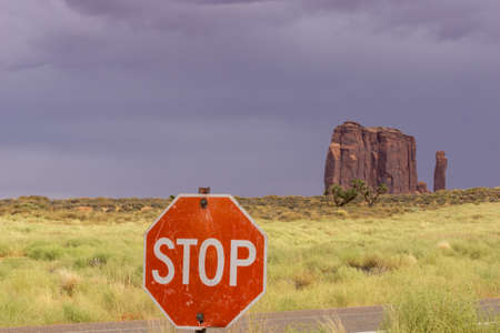 Sunlight highlights flat land and grass with sharp rock outcrop beyond stop sign in Monument Valley Utah USA.の写真素材