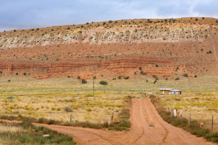Utah landscape with huge mesa landform dominating small buildings and dirt road running two diretions.の写真素材
