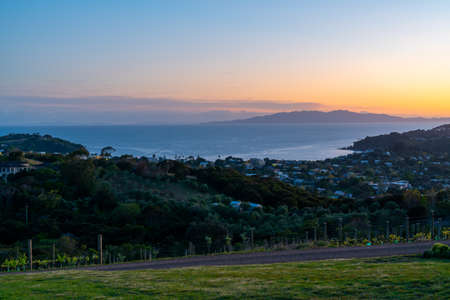 View across Waiheke Island township and sea to the Coromandel peninsula under a golden glow at sunrise, New Zealand.の写真素材