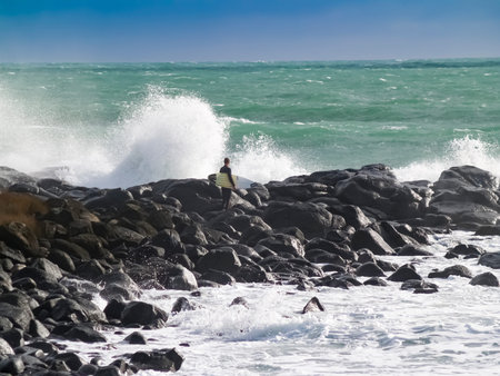 Raglan New Zealand - June 7 2008 - Lone surfer stands holding his board waiting for moment to jump...