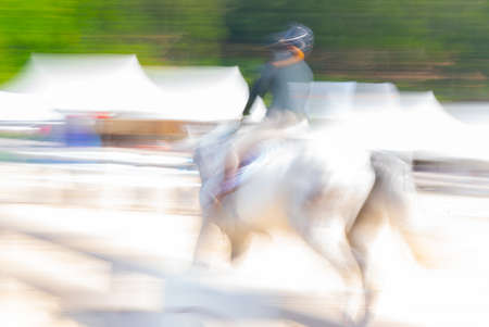 Abstract white horse and rider blurred in motion conveying speed and action.の写真素材