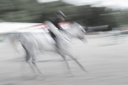 Abstract white horse and rider blurred in motion conveying speed and action.