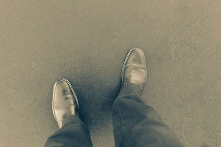 Personal point of view downward to pair of leather boots on concrete path in old-world split tone effectの写真素材