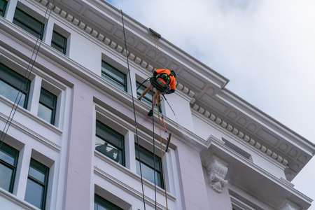 Wellington New Zealand - July 29 2021; Roped up abseiling the side of high building cleaner is working using water-blaster to wash the exterior.のeditorial素材