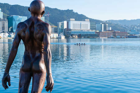 Wellington New Zealand - July 31 2021; Statue of naked man leaning into wind on city waterfront with commercial skyline behind installed in 2007 by sculpture Max Patte.のeditorial素材